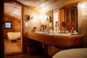A wooden bathroom with a large mirror, two sinks, and a wooden vanity. - Hotel Nufenen (Obergoms)