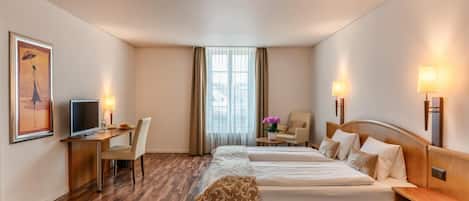 A hotel room with a bed, desk, chair, television, and a painting on the wall.