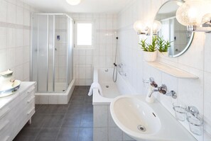 Ein modernes Badezimmer mit Duschkabine aus Glas, freistehender Badewanne, Waschbecken in Weiß und Spiegel mit runder Leuchte.
