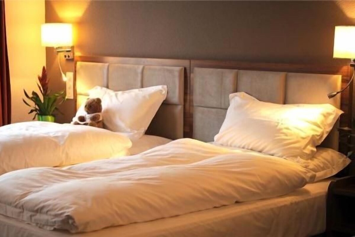A hotel room with a double bed, two bedside lamps, a nightstand, and a decorative plant.