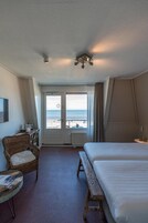 A hotel room with a bed, a chair, a desk, and a view of the beach.