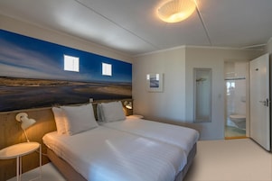 A bedroom with a large bed, bedside lamps, a wall-mounted picture, and a door leading to a bathroom.