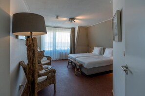 Una habitación de hotel con una cama, una silla, una lámpara y un ventanal con cortinas.
