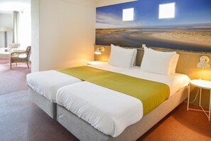 Habitación de hotel con cama, dos lámparas de noche, vistas de un paisaje por la ventana y un área de descanso con sillas.