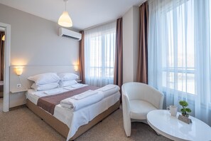 A hotel room with a bed, bedside lamps, a chair, a small table with a plant and a cup, and large windows with curtains. - Blue Label Apart House (Sofia)