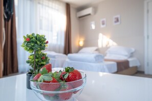 A hotel room with a bed, a bedside table with a bowl of strawberries, and a potted plant. - Blue Label Apart House (Sofia)