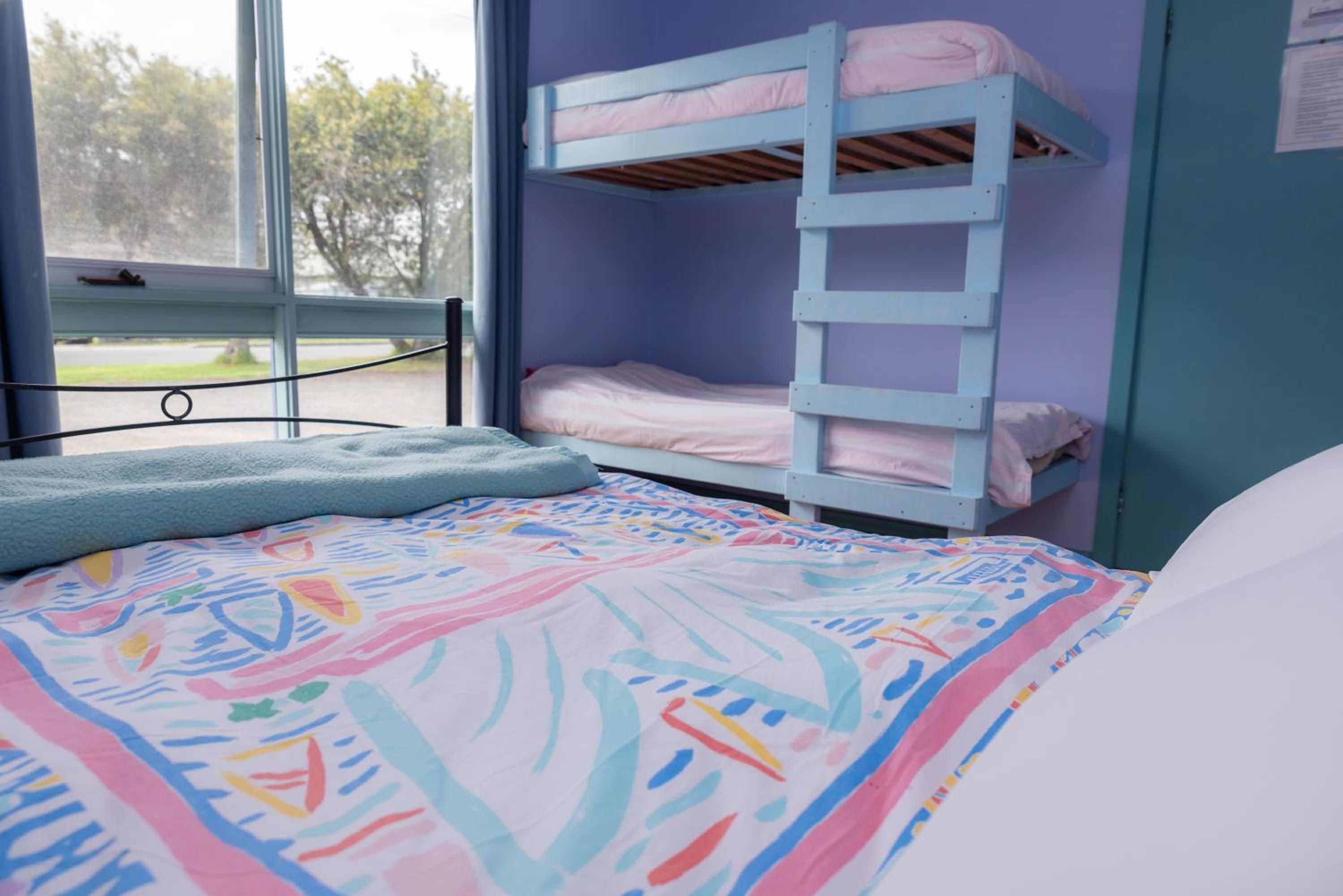 Una cama litera con escalera, una ventana que da a vistas de árboles y una colcha de colores.