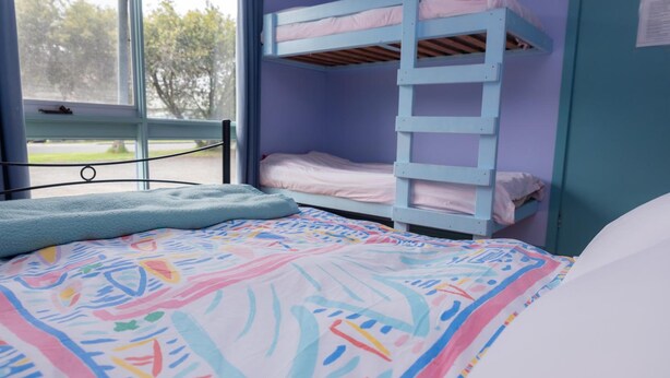 Uma cama beliche com escada, janela com vista para árvores e um edredom colorido.