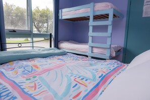 A bunk bed with a ladder, a window with a view of trees, and a colorful bedspread. - Anglesea Backpackers (Anglesea)