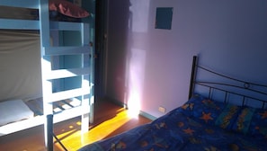 Quarto com beliche, uma cama de solteiro e janela que permite entrada de luz natural.