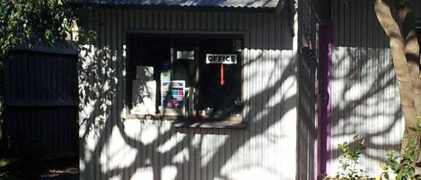 A small office with a corrugated metal roof, a window with an 'OFFICE' sign, and a potted plant in the foreground.
