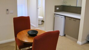 A compact kitchen with a dishwasher, a small countertop, and a dining area with a round table and two chairs. - Allansford Hotel Motel (Allansford)
