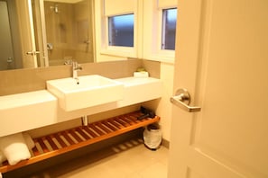 Un baño con dos lavamanos, un espejo, una ducha y un perchero para toallas.