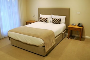 Una habitación de hotel con una cama grande, una mesita de noche con un teléfono y una lámpara.