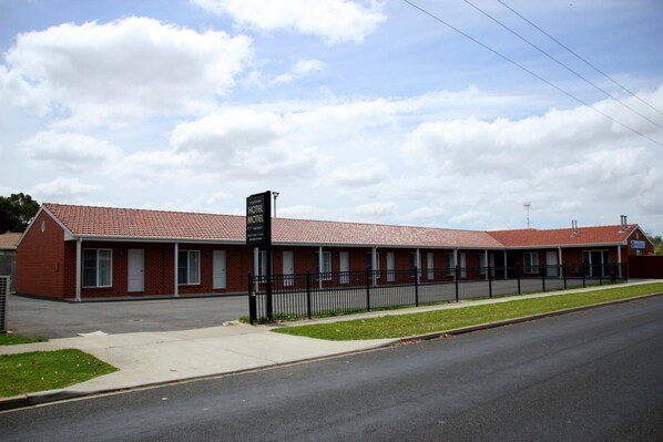 Un motel con techo de tejas rojas, cerca negra y un cartel que indica habitaciones disponibles.