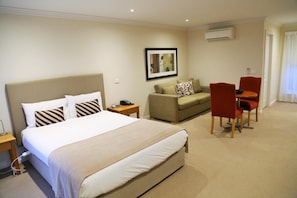 Habitación de hotel con una cama, un sofá, una silla, una mesita pequeña y un equipo de aire acondicionado.