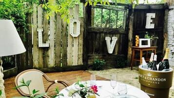 An outdoor dining area with a wooden fence, a table set with plates, glasses, and a vase of flowers.