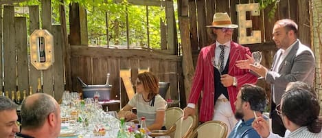 Un área de comedor al aire libre con mesas dispuestas para una comida, rodeada por una valla de madera y follaje.