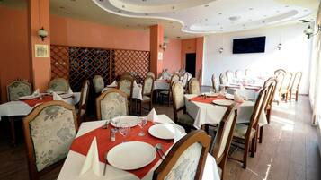 A restaurant with multiple tables, each set with white tablecloths and red napkins, featuring classic wooden chairs with floral upholstery.