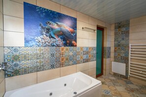 Casa de banho com uma banheira grande, chuveiro e parede revestida com um mural de tartaruga-marinha.