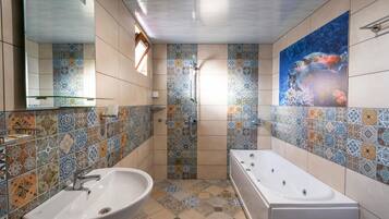 A bathroom with a large bathtub, a sink, and a shower. The walls are tiled with a patterned design.