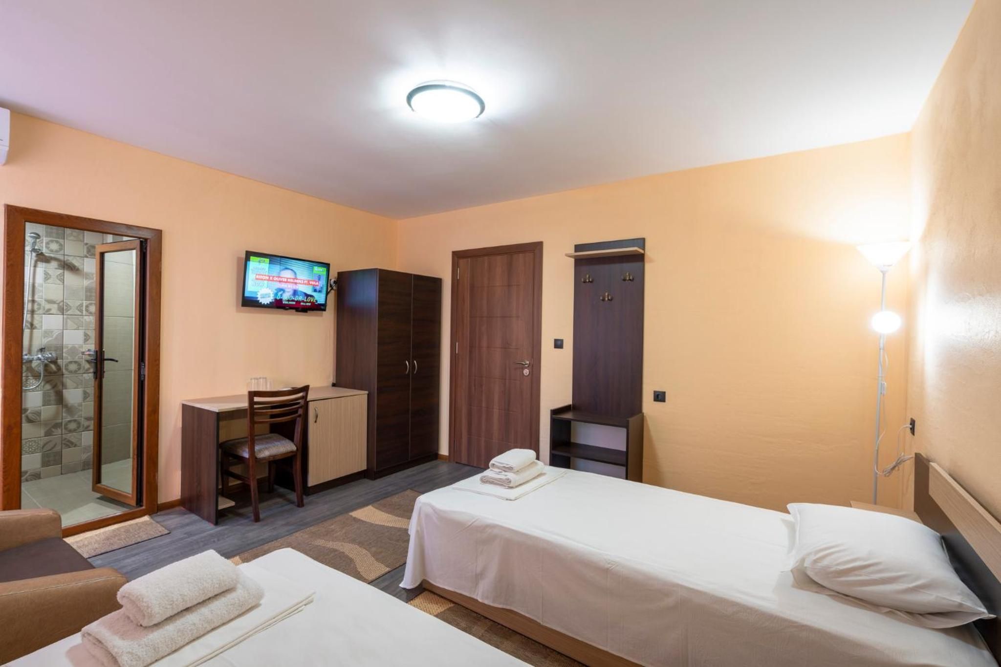 A hotel room with a shower, a desk, two beds, and a TV.