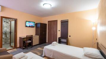 A hotel room with a shower, a desk, two beds, and a TV.