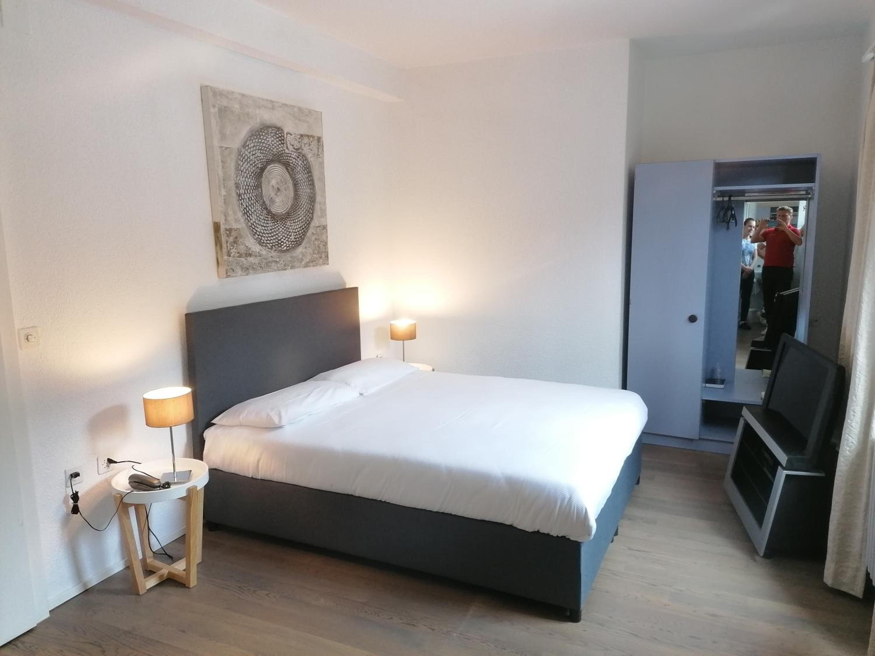 Ein Schlafzimmer mit einem Bett, Nachttischlampen, einem kleinen Tisch, einem Wandbild und einer Tür zu einem Badezimmer.