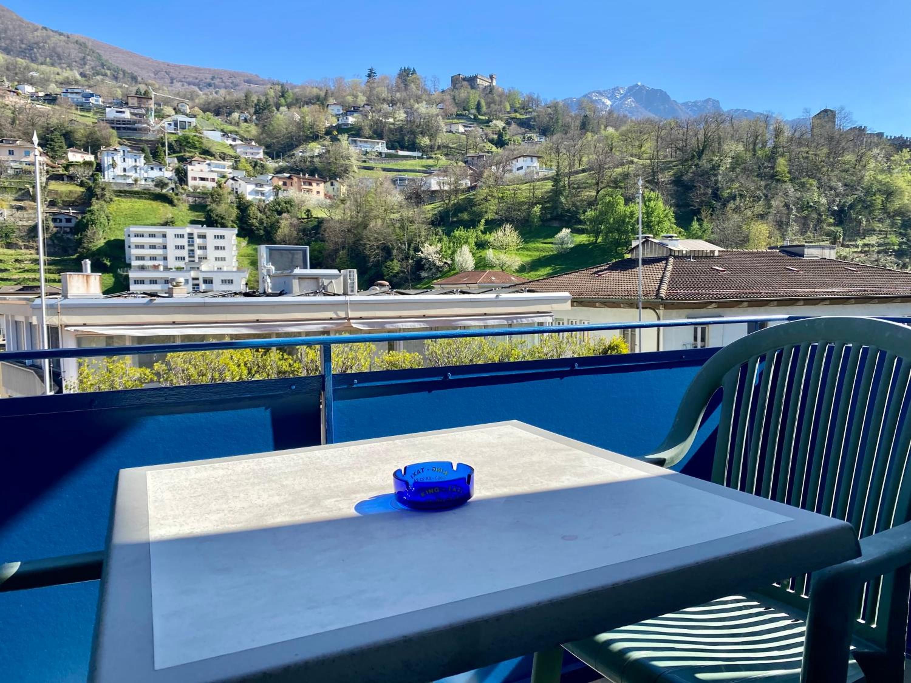 Ein Balkon mit Tisch und Stuhl, der Blick auf einen Hügel mit Gebäuden und einer Burg freigibt.