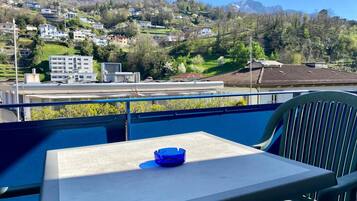 Ein Balkon mit Tisch und Stuhl, der Blick auf einen Hügel mit Gebäuden und einer Burg freigibt.
