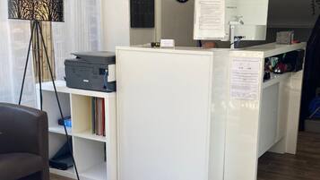Ein moderner Arbeitsraum mit Schreibtisch, Computer und Drucker. An der Wand hängt eine Uhr und in der Ecke steht eine Pflanze.