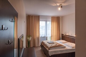 Habitación de hotel con cama, mesita de noche, espejo, ventana con cortinas e iluminación en el techo.
