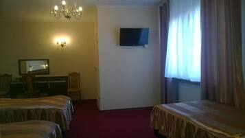 A hotel room with two beds, a television, a desk with a chair, a chandelier, and a window with curtains.