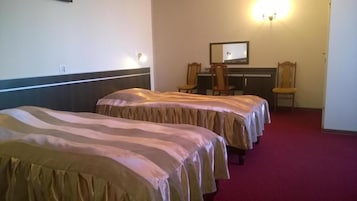 Una habitación de hotel con dos camas individuales, un escritorio con silla y un espejo en la pared.