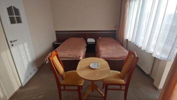 A hotel room with two single beds, a small round table with a single chair, and a door with a window.