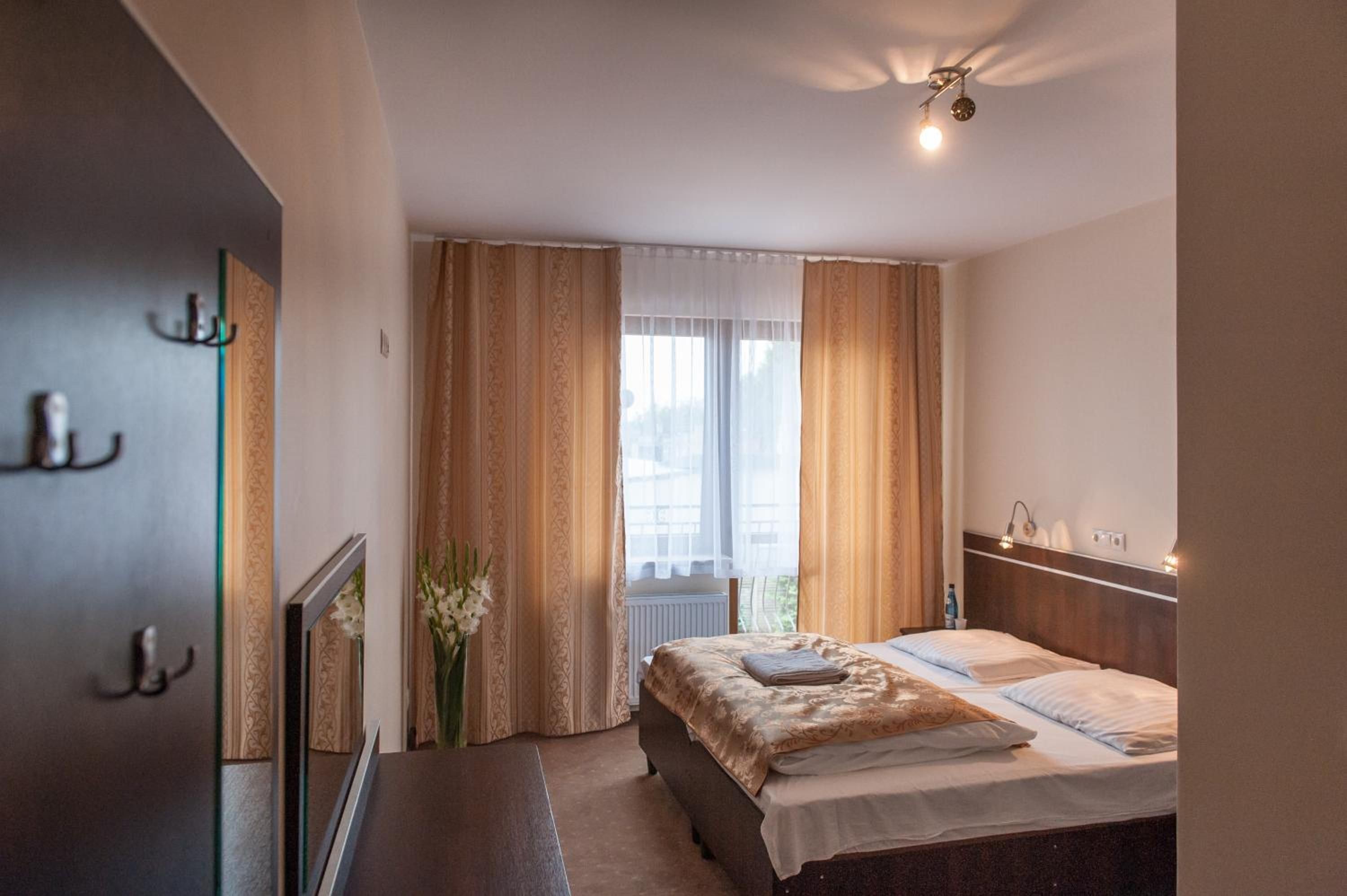 Een hotelkamer met een bed, nachtkastje, spiegel, raam met gordijnen en een plafondlamp.