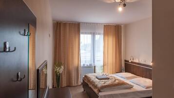 A hotel room with a bed, a bedside table, a mirror, a window with curtains, and a ceiling light.