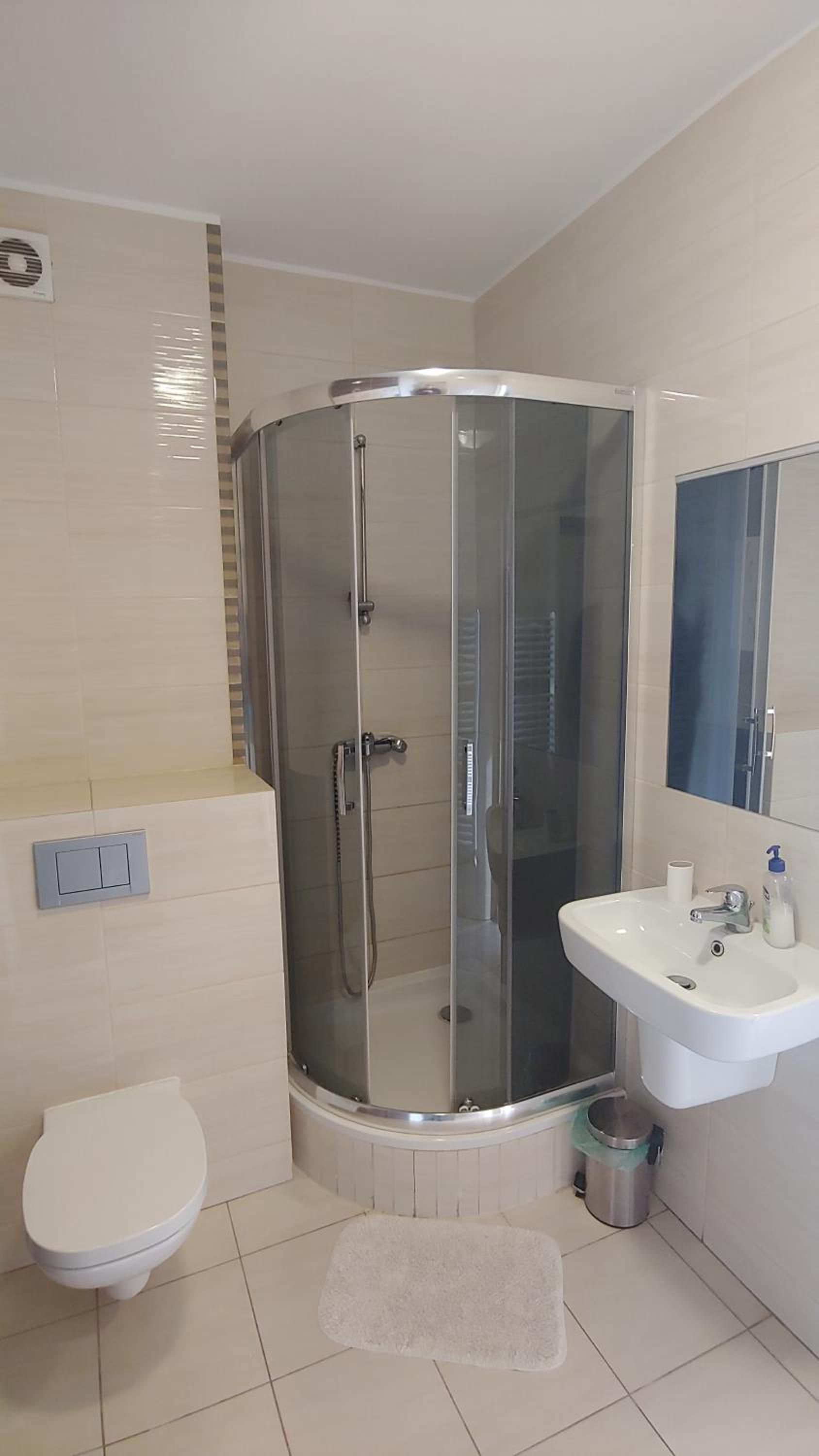 A modern bathroom with a glass-enclosed shower, a white toilet, and a sink with a mirror.