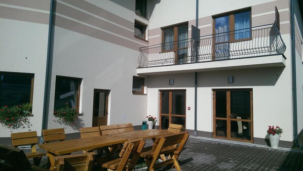 A two-story building with a balcony, wooden furniture, and potted plants.