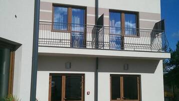 A two-story building with a balcony, large windows, and a paved courtyard.
