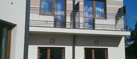 A two-story building with a balcony, large windows, and a paved courtyard.