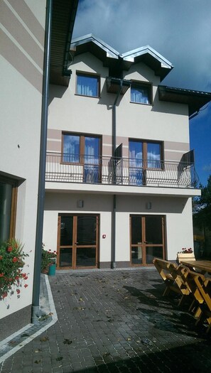 A two-story building with a balcony, large windows, and a paved courtyard.