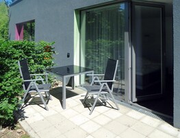 Un patio con una mesa y sillas de vidrio, una puerta corrediza de vidrio y un ventanal con cortinas.