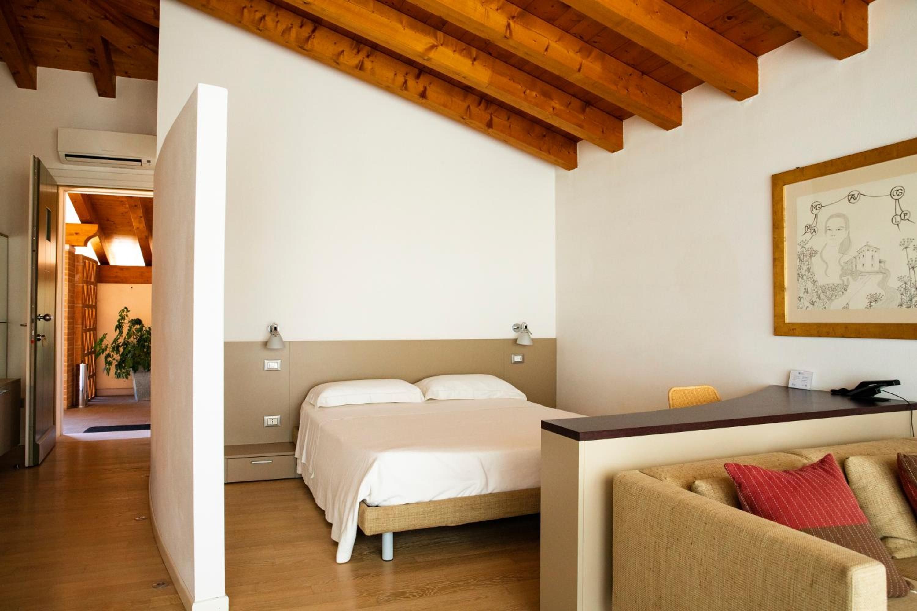 A bedroom with a bed, bedside lamps, a desk, a chair, and a painting on the wall.