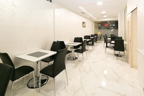Un espace de restauration propre et moderne, avec un sol en marbre blanc et des chaises noires. Les tables sont disposées en rangées, laissant un couloir dégagé au centre.