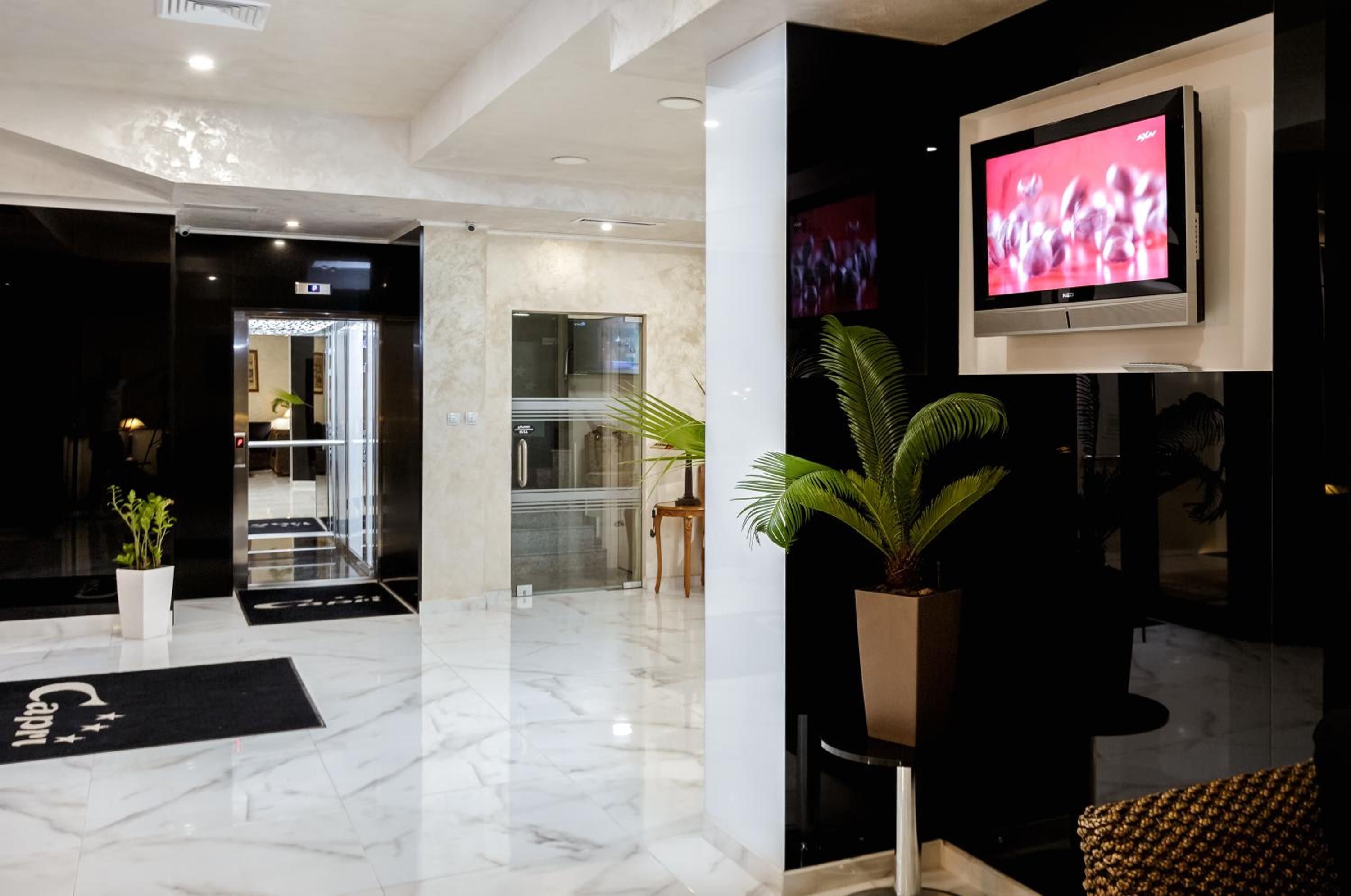 A modern lobby with a marble floor, a reception desk, a potted plant, and a flat-screen TV mounted on the wall.