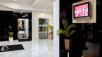 A modern lobby with a marble floor, a reception desk, a potted plant, and a flat-screen TV mounted on the wall.