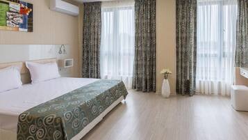 A hotel room with a large bed, a bedside table, a chair, and a window with curtains.