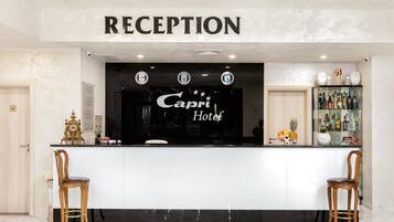A reception area with a marble floor, two wooden chairs, a reception desk, and a clock above the desk.