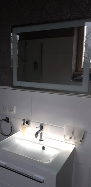 A bathroom with a white sink, a mirror, and two wall-mounted cups. - Schlossgut Gorow (Satow)